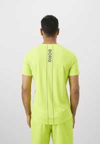 Mees, kes kannab neoonrohelist spordipusa ja lühikesi pükse, selg kaasas, seljal vertikaalne "BORG" tekst ja kaks musta joont.
