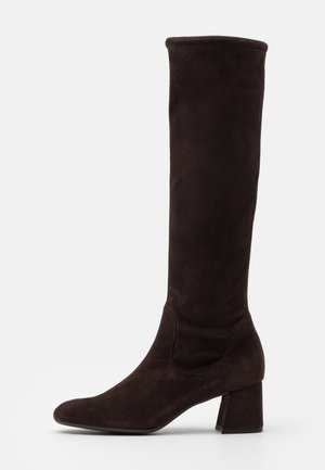 Botte haute en daim marron foncé avec talon bloc et bout arrondi, longueur jusqu'aux genoux, vue de côté sur fond blanc.