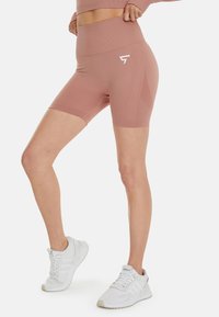 Stofroze high-waisted fietsshorts van rekbaar materiaal met ribbelstructuur en accentdetails aan de zijkant, gecombineerd met witte sport schoenen.