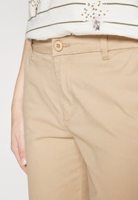 Khaki nohavice vyrobené z bavlny. Majú predné zapínanie na gombík, pútka na opasok a bočné vrecká. Textúrovaná tkanina s hladkým povrchom.