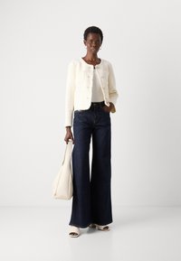 White cropped jacket with two front pockets, paired with dark wide-leg jeans, off-white handbag, and open-toe white heels.