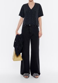 Černý krátký rukáv top s výstřihem do V a rozptýlenými ozdobami, spárovaný s širokými černými džíny. Doplněno žlutou kabelkou a texturovanými pantoflemi.
