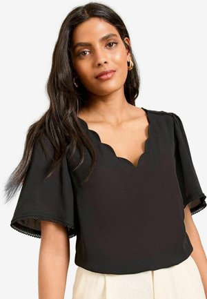 Blusa nera con scollatura a scallop e maniche corte a sbuffo. Presenta una rifinitura in pizzo ai bordi delle maniche, realizzata in un tessuto morbido.