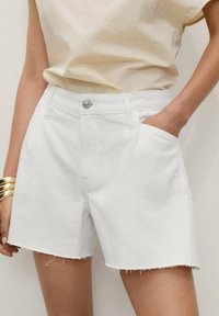 Shorts din denim alb cu margine destructurată, av�ând buzunare laterale și închidere cu un nasture argintiu. Asortați cu un top de culoare bej deschis.