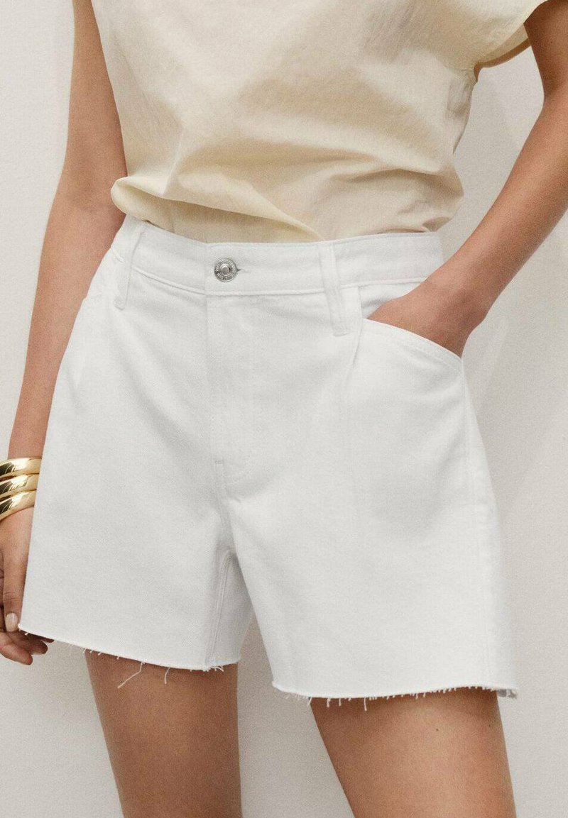 Shorts din denim alb cu margine destructurată, având buzunare laterale și închidere cu un nasture argintiu. Asortați cu un top de culoare bej deschis.