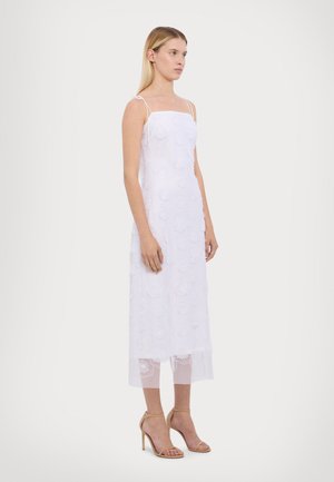 White embroidered midi dress with thin straps, featuring floral patterns, a sheer lower hem, and paired with beige high-heeled sandals.