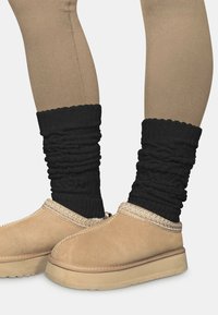 Beige Wildleder-Hausschuhe zum Hineinschlüpfen mit einer strukturierten, braunen Sohle, kombiniert mit gerafften schwarzen Strick-Stulpen.