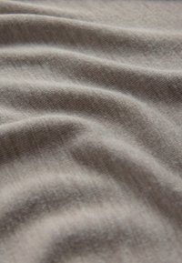 Miękki beżowy materiał o delikatnej dzianinowej teksturze, ukazujący łagodne fałdy i subtelne cienie na powierzchni.