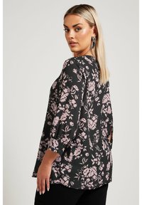 Svart blommig blus med rosa och vita blommönster, trekvartslånga ärmar, lös passform och strukturerad tyg.