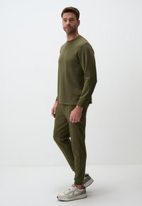Olive green sweatshirt and matching pants made of spandex-blend fabric, featuring long sleeves and tapered legs. White sneakers complete the outfit.