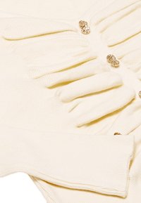 Maglione color crema con costine testurizzate, eleganti bottoni dorati e dettagli a costine su polsini e orlo. Tessuto morbido e lavorato a maglia.