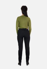 Jeans negros de cintura alta con un corte ajustado, combinados con una camiseta de manga larga verde. La camiseta presenta un escote redondo y una tela ligeramente texturizada.