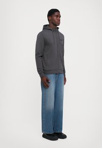 Gray zip-up hoodie made from soft fabric, featuring a front pocket, worn with light blue wide-leg jeans and black shoes.