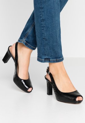 Czarne sandały na obcasie z odkrytymi palcami, z fakturą skóry krokodyla, błyszczącym wykończeniem i masywnym obcasem. Połączone z krótkimi niebieskimi dżinsami.