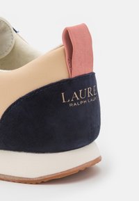 Sneakers med en marinblå mockaläpp, persikofärgad läderdetalj, krämfärgad krage och en gummisula med strukturerat grepp. Guldlogotyp finns.