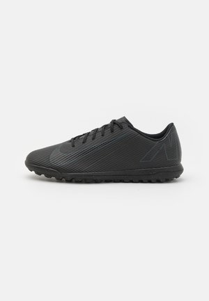 Schwarzer, niedrig geschnittener Sportschuh mit strukturierter Oberfläche, Schnürdesign und Gummisohle mit kleinen Noppen, von der Seite auf weißem Hintergrund gezeigt.