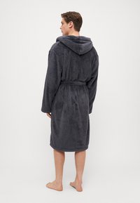 Hettebadekåpe i mørkegrått, laget av mykt, fluffy materiale. Har midjebånd, lange ermer og en strukturerte overflate.