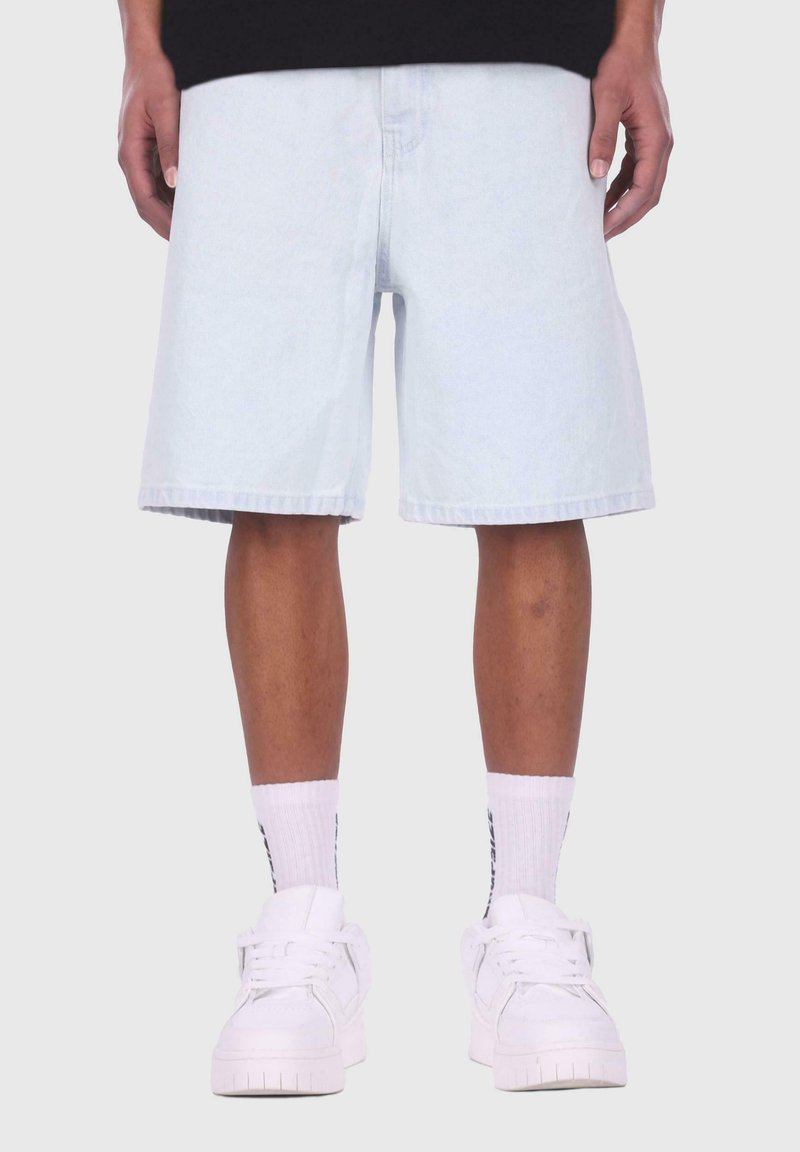 Light blue denim shorts with a straight cut, cuffed hems, and visible stitching details. Paired with white sneakers and striped socks.