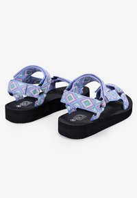 Sandalias coloridas con patrones, con diseños de tiras geométricas en azul, rosa y verde, suelas planas negras y una superficie texturizada.