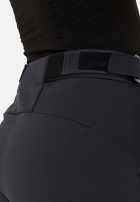 Zwarte broek met een gladde, matte textuur, voorzien van een klittenbandsluiting en een op maat gemaakt ontwerp. Heeft contrasterende paneeldetails aan de achterkant.