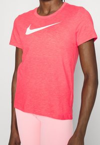 Camiseta coral de Nike con cuello redondo y manga corta. Presenta un logo swoosh blanco prominente en la parte frontal. Material suave y ligero.