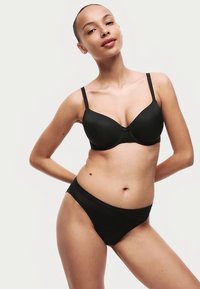 Černá podprsenka s hladkým povrchem, s kosticemi a nastavitelnými ramínky, doplněná o sladěné kalhotky s nízkým pasem. Oba kusy mají minimalistický design.