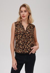 Top senza maniche marrone con motivo leopardato in nero. Tessuto leggero e morbido, con colletto e vestibilità comoda, abbinato a pantaloni neri.