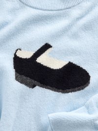 Vaaleansininen neulepaita, jossa on kudottu mustavalkoinen kenkäkuvio. Kengällä on pyöreä kärki ja remmi jalkapöydän kohdalla.