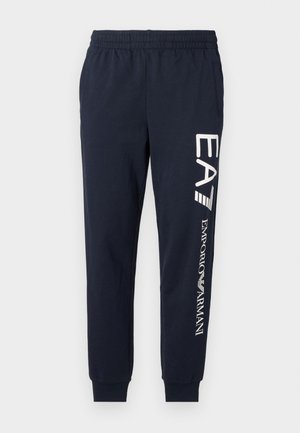 Pantaloni jogger in cotone blu navy con vita elasticizzata, gambe affusolate e loghi EA7 ed Emporio Armani bianchi contrastanti stampati lungo il lato.