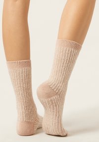 Calze lavorate a maglia in una morbida tonalità rosa con una texture a coste, caratterizzate da strisce chiare e scure. Il design include polsini spessi e talloni rinforzati.