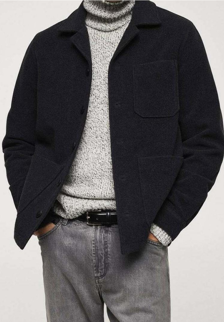 Giacca in misto lana blu navy con colletto, bottoni a pressione e taschino sul petto, indossata sopra un dolcevita grigio chiaro in maglia e abbinata a jeans grigi.