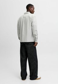 Camisa de manga larga gris claro con cuello, combinada con pantalones vaqueros anchos oscuros. Material de mezcla de algodón con una textura suave.