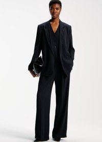 Navy pinstriped tailored suit with wide-leg pants and a double-breasted blazer, paired with a black clutch bag, worn over a matching top.