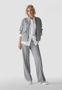 Gray athletic jacket with two front pockets, paired with gray wide-leg pants and a white shirt. Lightweight fabric, simple design.