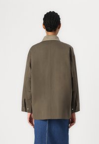 Olivově zelená oversized bunda se světlým límcem. Má dlouhé rukávy, rovný střih a viditelné knoflíky na manžetách.