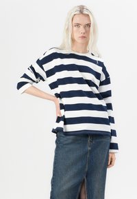 Navy and white striped long-sleeve shirt, relaxed fit, lightweight fabric, complemented by a denim skirt with a front slit.