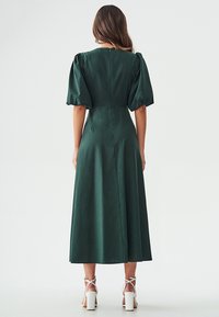 Green midi dress with puffed short sleeves, a fitted bodice, and flowing skirt; made from smooth fabric with a natural sheen.