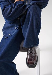 Scarpe in pelle bordeaux con suola in gomma nera, design con lacci e finitura lucida. Indossate con pantaloni in denim blu larghi e giacca.