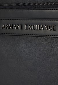 Borsa in pelle nera con logo "ARMANI EXCHANGE" in rilievo. Superficie testurizzata con cuciture a contrasto e chiusura a zip.