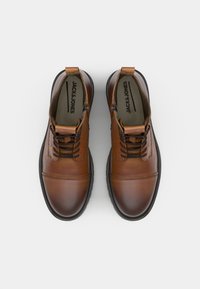 Zapatos de cuero marrón con un acabado liso, que presentan cordones, detalles de costura y un cuello acolchado. Suela de goma negra con tracción.