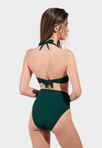 Tamnozeleni bikini set s halter vratom i vezanjem te visokim donjim dijelom. Glatka, rastezljiva tkanina s minimalnim detaljima.