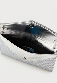 Stříbrná psaníčko s uzávěrem na cvok, texturovaným předním panelem a černým interiérem, který obsahuje zipovou kapsu a štítek značky.