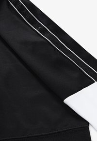 Black athletic fabric with a white cuff, featuring a contrasting stripe along the side. Smooth texture, no distinct patterns or hardware.