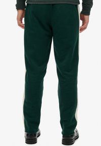 Grüne Baumwoll-Sweatpants mit schlankem Schnitt, mit kontrastierenden beigen Seitestreifen und elastischen Bündchen, kombiniert mit schwarzem Schuhwerk.