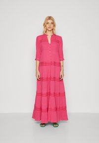 Vestido longo rosa feito de tecido leve, com fechamento frontal em botões, mangas três quartos e detalhes texturizados em acentos horizontais.