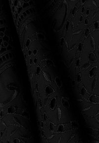 Tessuto nero ricamato con intricate fantasie floreali e fogliari, con una texture morbida e motivi intagliati visibili in tutto lo sfondo.