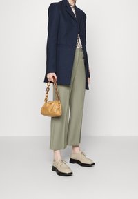 Námornícky vlněný blazer, vzorovaná béžová halenka, olivově zelené široké kalhoty, béžové boty s černými podrážkami a malá žlutá kabelka s řetízkem.