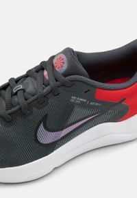 Baskets de course Nike en maille gris foncé avec des accents rouges, dotées d'un swoosh violet, d'une surface texturée et de détails de marque visibles.