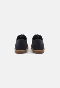 Des chaussures bleu marine avec une tige en tissu texturé et une semelle en caoutchouc marron, présentant un design classique à profil bas et des talons arrondis.