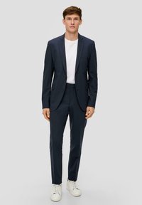 Marineblaues, tailliertes Anzug mit Slim-Fit, einreihigem Blazer, passender Hose, weißem T-Shirt darunter und weißen Sneakers. Glatte Stofftextur.